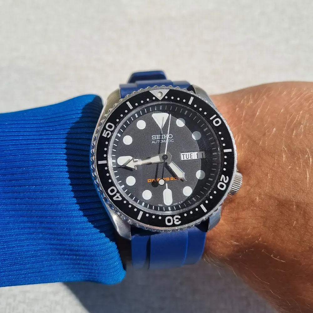 En handled som bär en blå tjocktröja med en Seiko SKX007 med blått gummi klockarmband