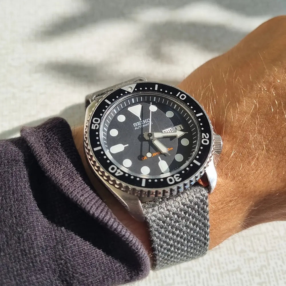En handled som bär en Seiko SKX007 som sitter på ett grått ribbat natoband