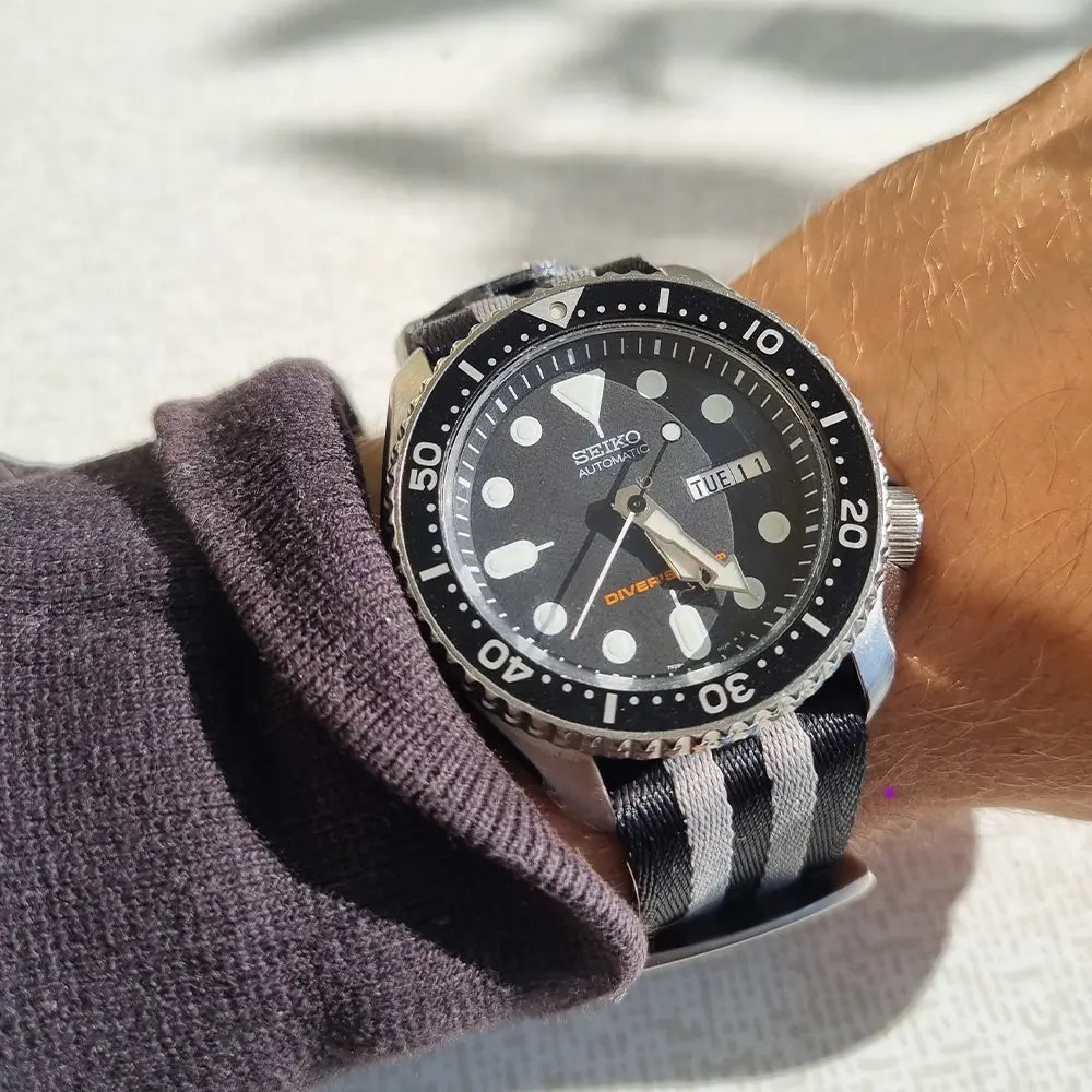 En handled som har en Seiko SKX007 med ett natoband med gråa streck på sig