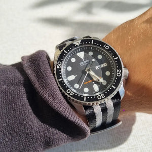 En handled som har en Seiko SKX007 med ett natoband med gråa streck på sig