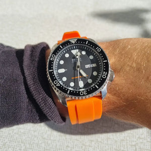 En Seiko SKX007 med oranget klockarmband av gummi på handled
