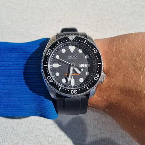 En Seiko SKX007 med svart klockarmband av läder på vristen med blå tröja